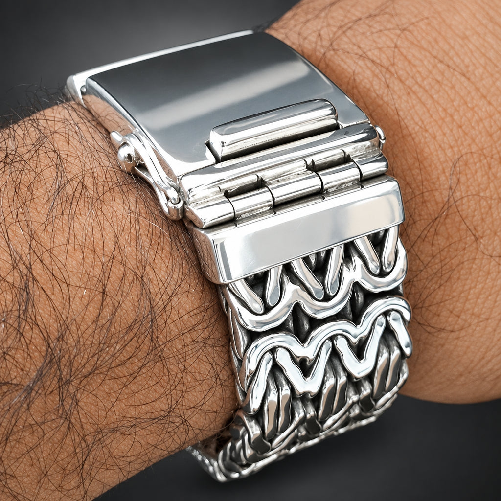 A close-up of a silver-toned metal link watch band worn on a person's wrist, showing the clasp and textured wavy links against dark skin and a black background.