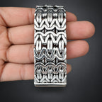 Silver bracelet with intricate pattern held in a hand against a dark background