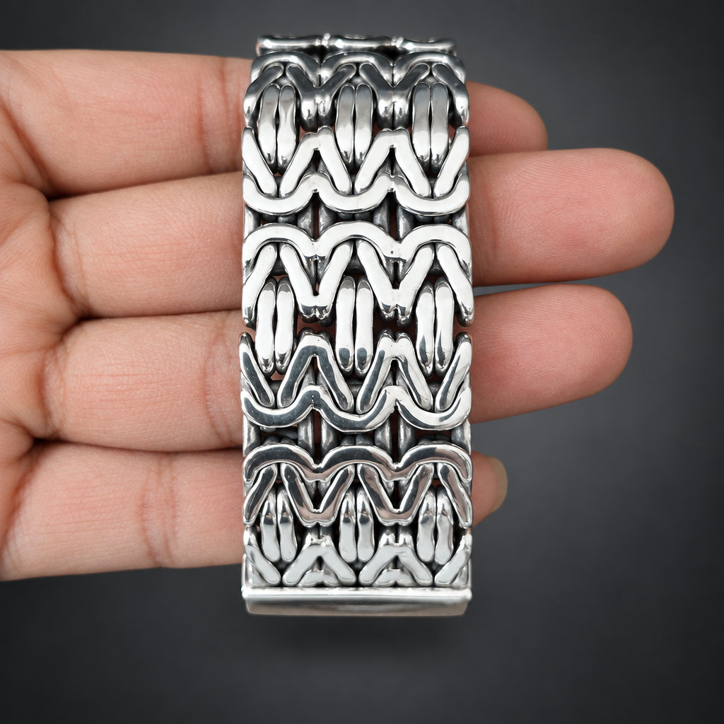 Silver bracelet with intricate pattern held in a hand against a dark background