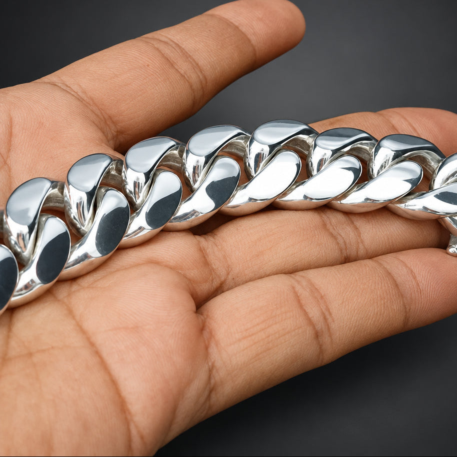 A close-up of a hand holding a chunky, highly polished silver Cuban link chain bracelet against a dark gray background.