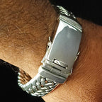 A close-up of a silver-toned metal link bracelet watch being worn on a person's wrist against a dark background.
