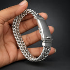 Silver chain bracelet held in a hand against a dark background