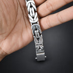 Silver bracelet with intricate design held in a hand against a dark background
