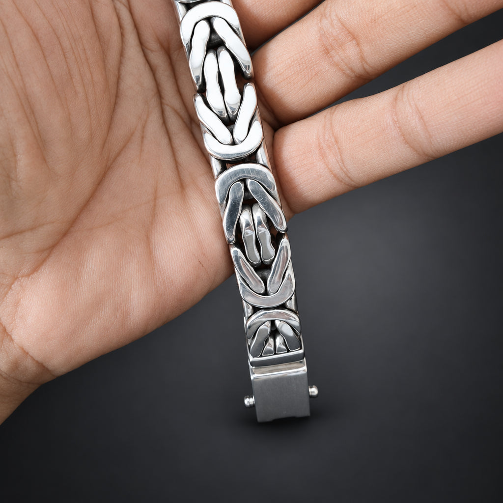 Silver bracelet with intricate design held in a hand against a dark background