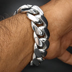 A close-up of a polished silver-tone Cuban link chain bracelet worn on a person's wrist.