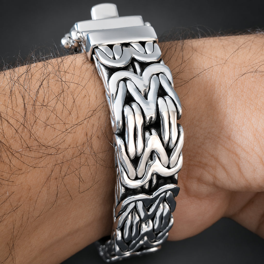 A close-up of a silver-toned metal bracelet with an intricate, interlocking textured pattern, worn on a person's wrist.
