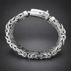 Silver braided bracelet held by a hand on a wooden surface with a dark background