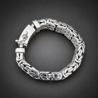 Silver bracelet with intricate design held in a hand against a dark background