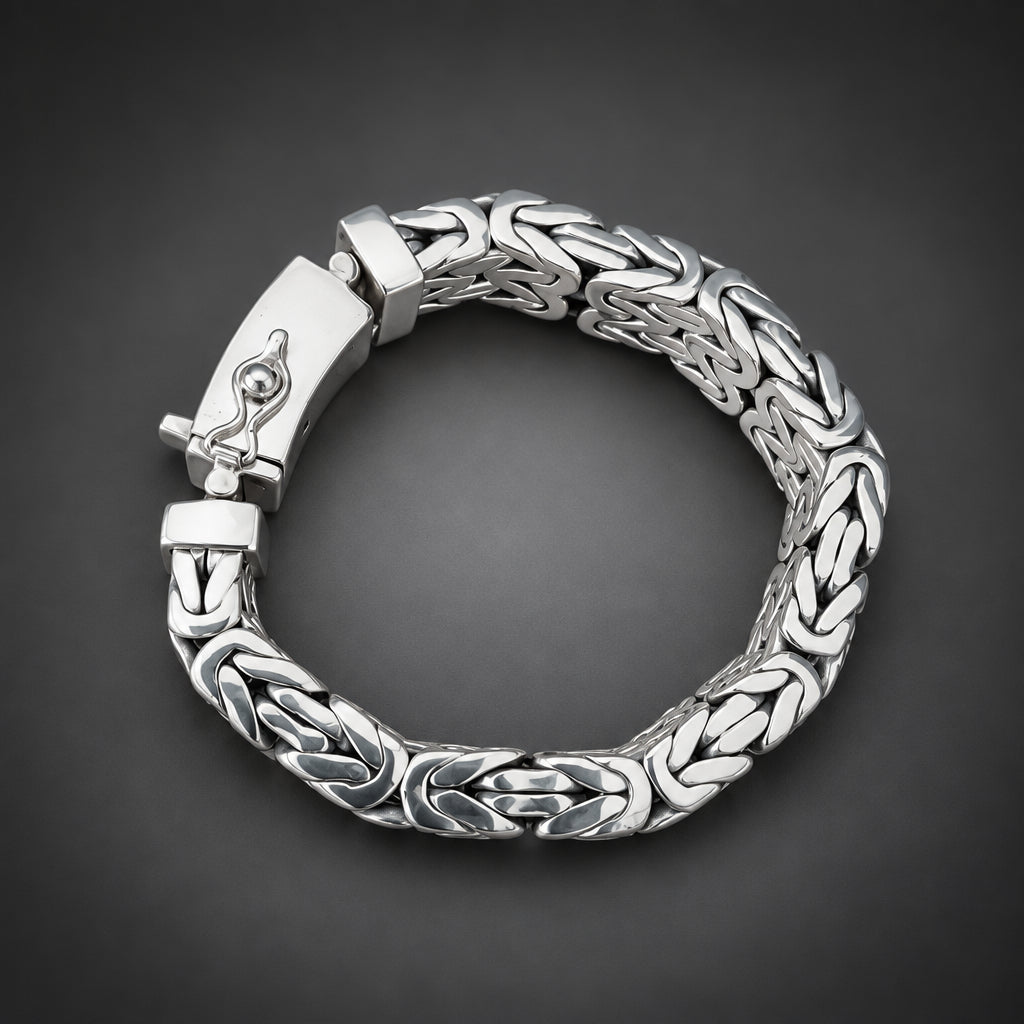 Silver bracelet with intricate design held in a hand against a dark background