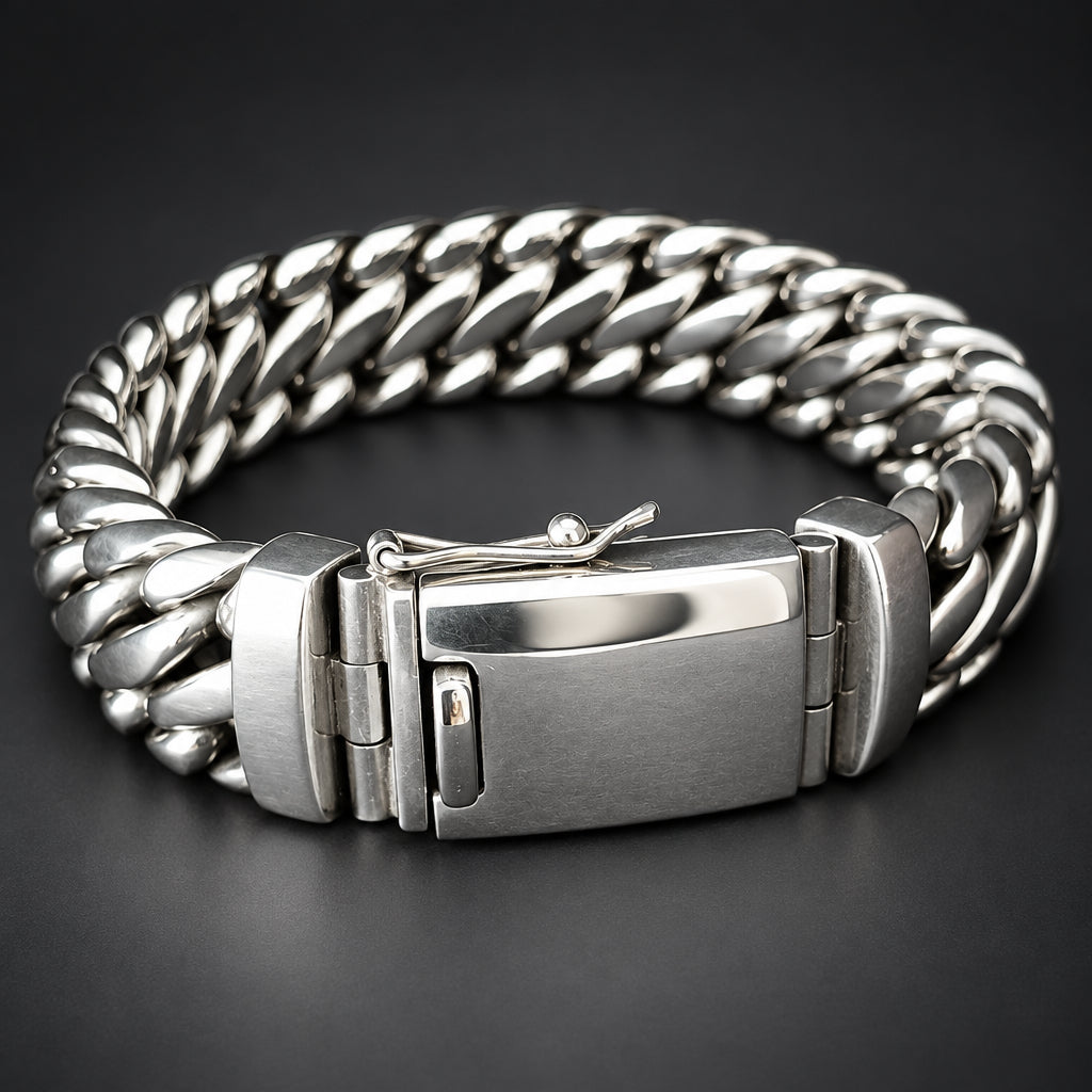 A silver stainless steel Cuban link bracelet with a brushed metal clasp, displayed on a dark gray background.