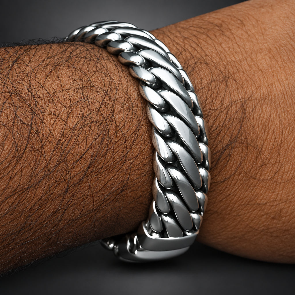 A close-up of a polished silver-toned Cuban link chain bracelet worn on a person's wrist, with the arm's dark hair visible against a dark gray background.