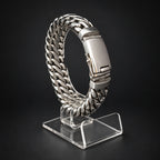 A silver stainless steel Cuban link chain watch band displayed on a clear acrylic stand against a dark black background.