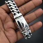 A close-up of a polished silver-tone stainless steel link bracelet being held in a person's hand, showing the textured links and clasp.