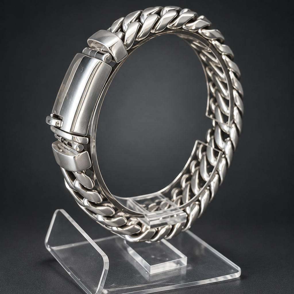 A silver-toned metal Cuban link bracelet displayed on a clear acrylic stand against a dark gray background.