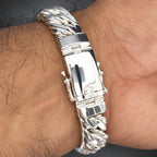 A close-up of a silver-toned metal bracelet worn on a person's wrist, featuring a polished rectangular clasp and a textured twisted link band.