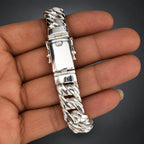 Silver bracelet held in a hand against a white background