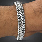 A close-up of a silver-toned metal bracelet with a textured, interlocking link design worn on a person's wrist.