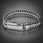 A silver-toned metal bracelet with a curb-style chain link design and a polished rectangular clasp, shown on a neutral gray background.
