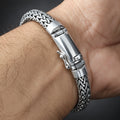 A close-up of a silver braided metal bracelet worn on a person's wrist, showing the woven chain and clasp in detail.