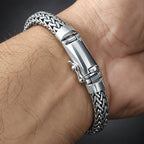 A close-up of a silver braided metal bracelet worn on a person's wrist, showing the woven chain and clasp in detail.