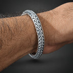 Silver bracelet on a wrist with a textured pattern against a dark background