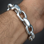 A close-up of a chunky silver chain bracelet worn on a person's wrist, showing the polished metal links against skin.
