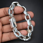 Silver chain bracelet held by a hand against a dark background