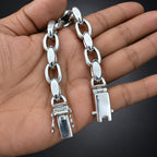 Silver chain bracelet held in a hand against a dark background