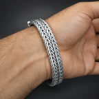 Silver bracelet with a textured pattern on a wrist against a dark background