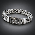 A silver-toned metal chain bracelet with an ornate engraved clasp, displayed on a gradient dark grey background.