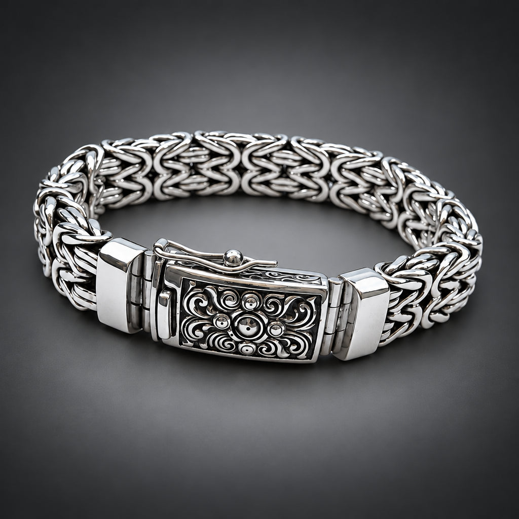 A silver-toned metal chain bracelet with an ornate engraved clasp, displayed on a gradient dark grey background.