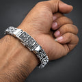 Silver bracelet with intricate designs on a wrist against a dark background