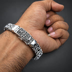 Silver bracelet with intricate designs on a wrist against a dark background