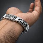 Silver bracelet with intricate design on a wrist against a gradient dark grey background