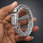 Silver bracelet with intricate designs held by a hand on a dark background