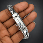 Silver and gold bracelet held by a hand against a dark background