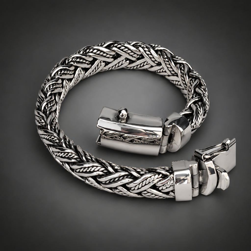 A silver-toned braided chain bracelet with a polished rectangular clasp, displayed on a neutral light gray background.