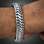 A close-up of a silver-toned metal chain bracelet worn on a hairy wrist.