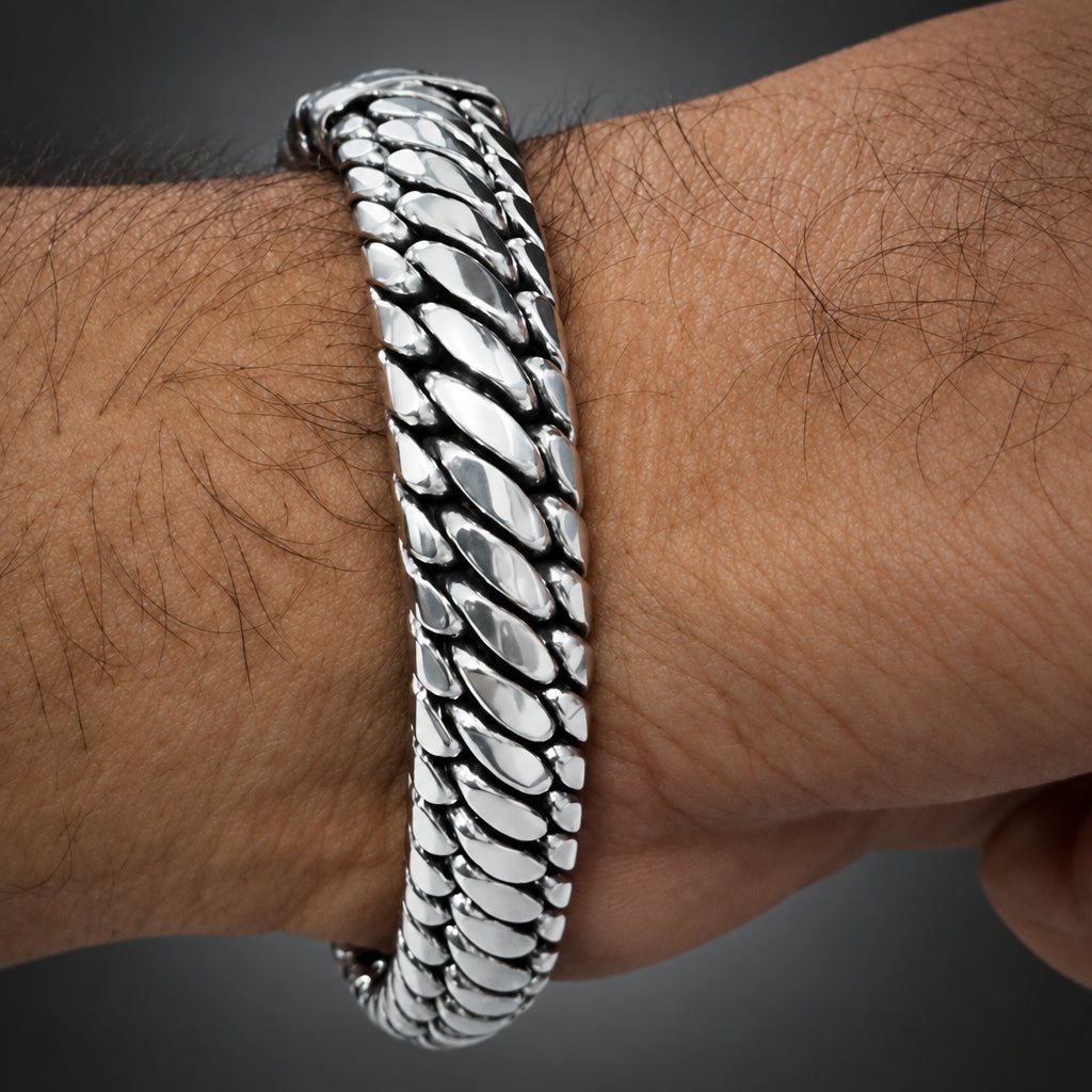 A close-up of a silver-toned metal chain bracelet worn on a hairy wrist.