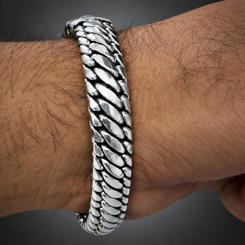 A close-up of a silver-toned metal chain bracelet worn on a hairy wrist.