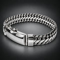A silver-toned metal bracelet with a curb-style chain link design and a polished clasp, photographed on a plain dark background.