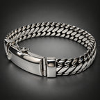 A silver-toned metal bracelet with a curb chain pattern and a polished clasp, shown on a neutral light gray background.