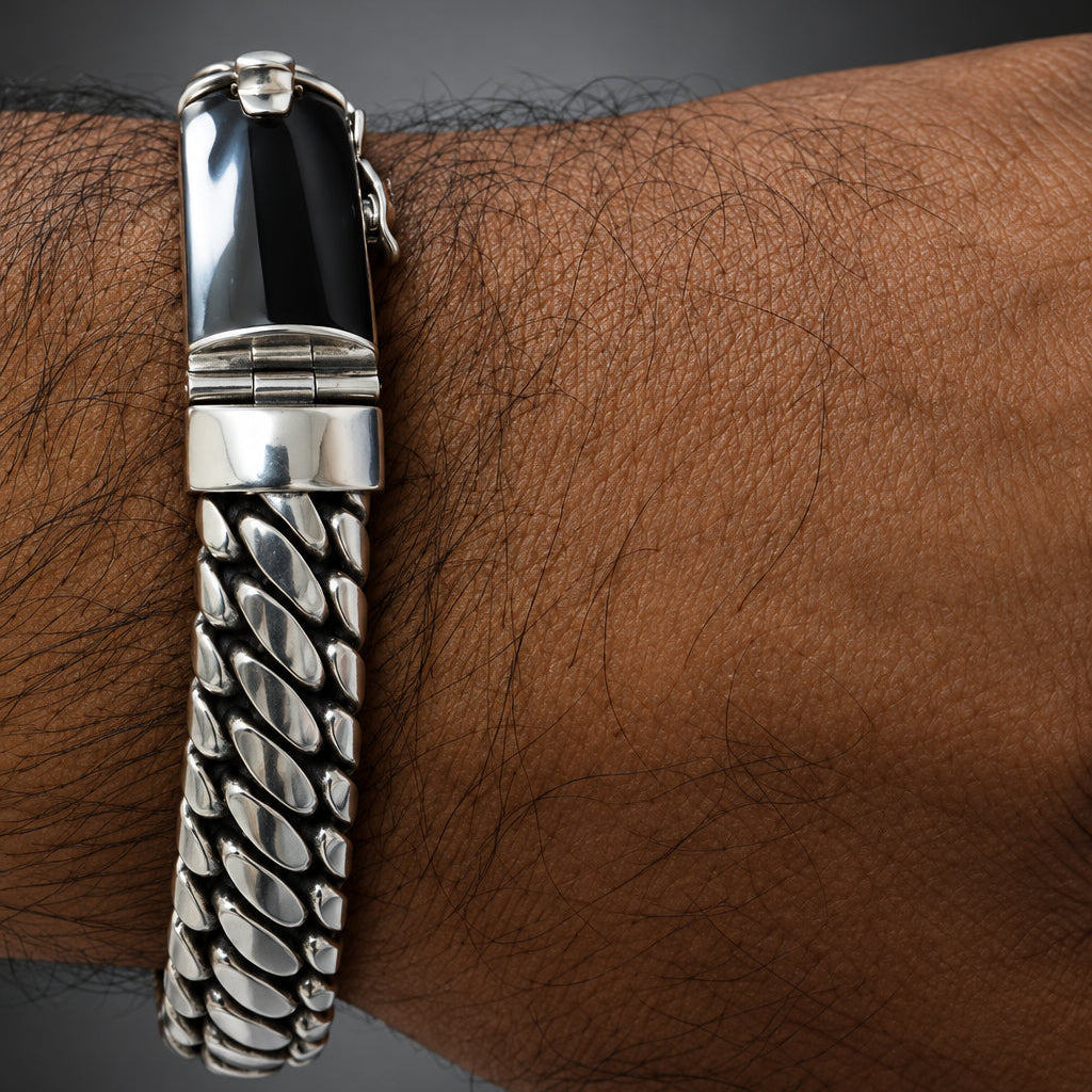 A men's silver-toned chain bracelet with a polished rectangular black inlay clasp, shown worn on a man's wrist against a dark gray gradient background.