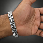 A close-up of a hand wearing a thick, polished silver Cuban link bracelet against a dark gray background.