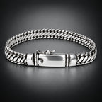 A silver-toned braided chain bracelet with a polished clasp, displayed on a neutral light gray background.