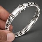 Silver bracelet held by a hand on a light background