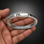 Silver bracelet held by a hand on a light gray background