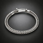 A silver braided cable bracelet with a polished clasp, displayed on a dark gray gradient background.