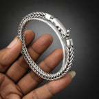 Silver bracelet held by a hand against a light gray background