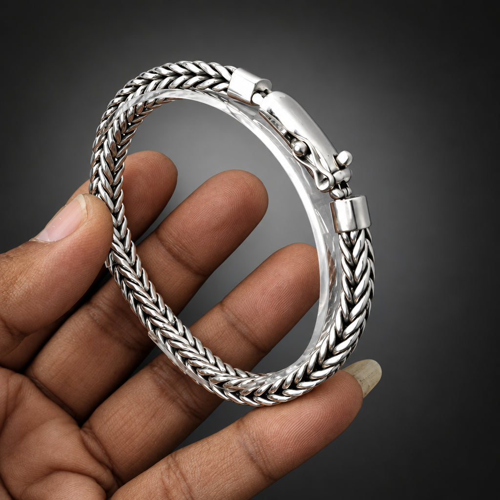 Silver bracelet held by a hand against a light gray background